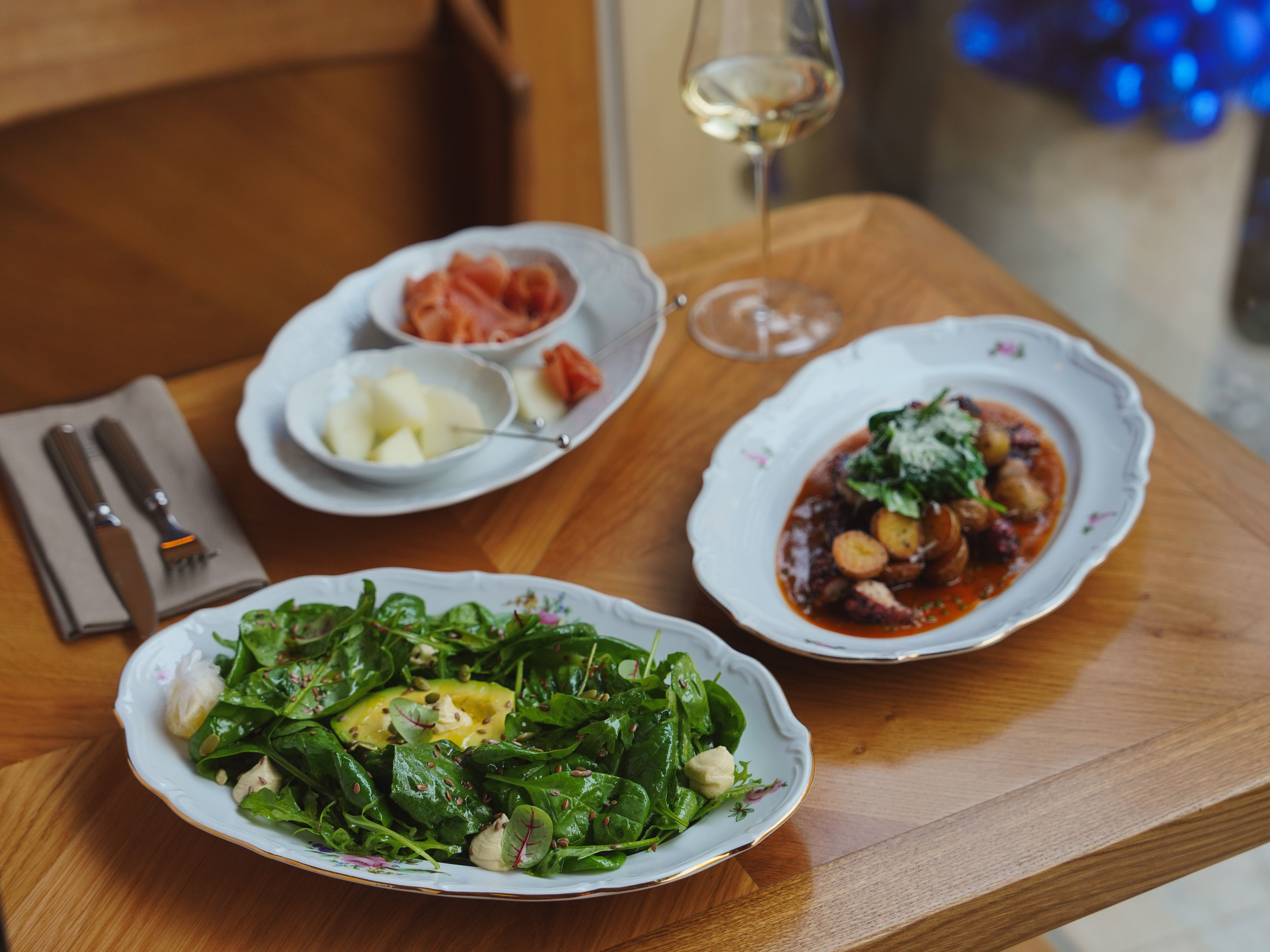 Elegant dining setup featuring salad, gourmet meal, and wine on a wooden table.