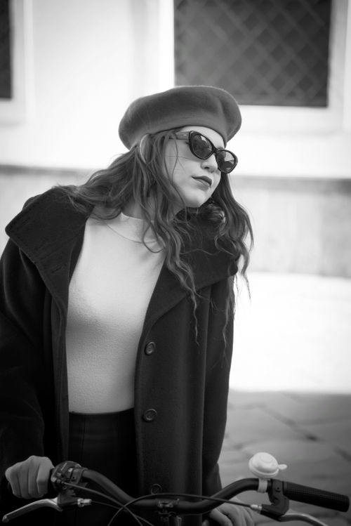 Free Monochrome fashion portrait of a woman in a beret and sunglasses biking outdoors. Stock Photo