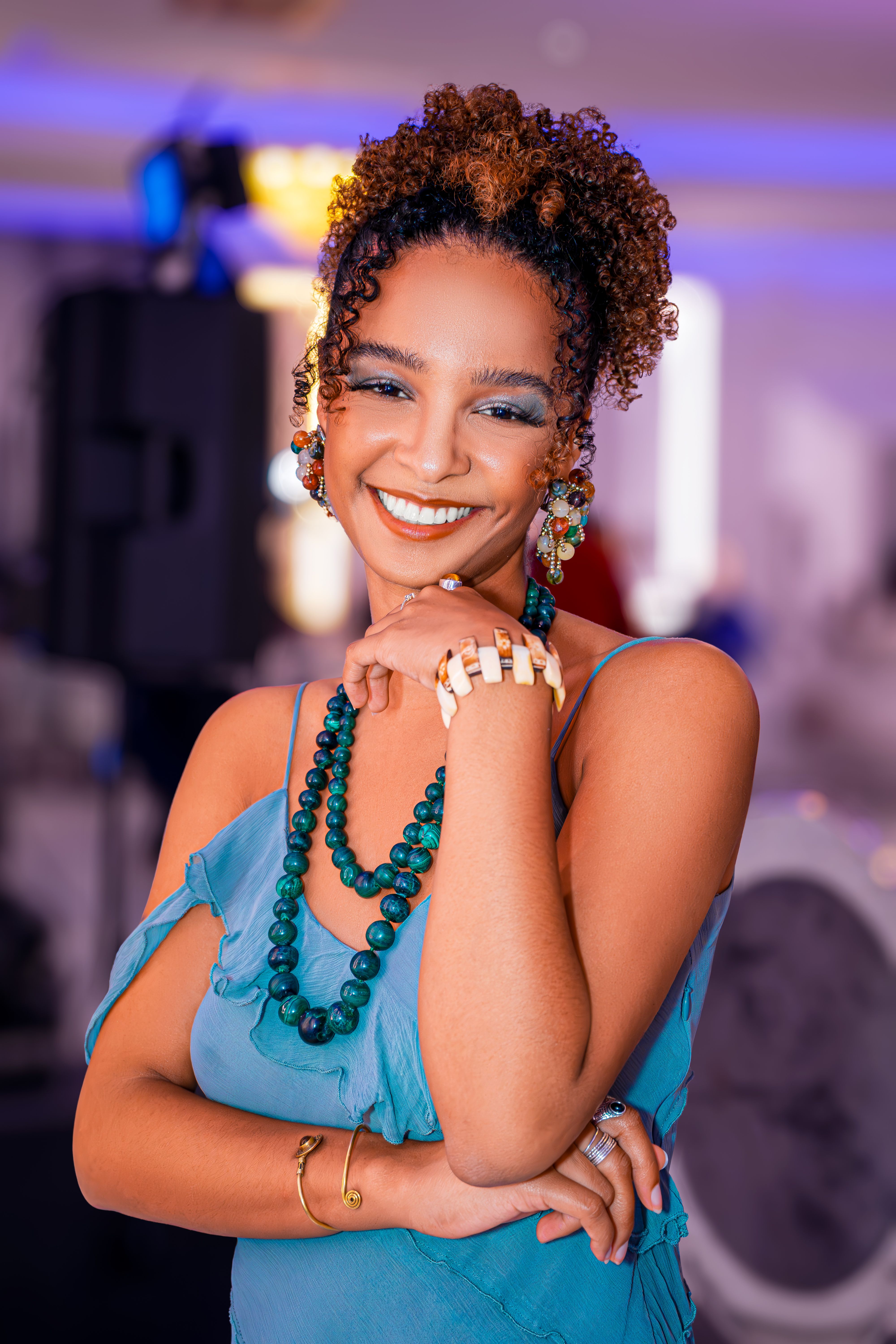 Portrait of a young woman in a blue dress, smiling with colorful accessories.
