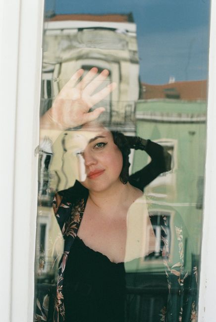 Reflective portrait of a woman standing behind a glass window in Lisbon, showcasing urban architecture.