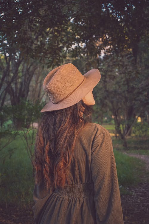 Woman in a Dress and Hat Standing in a Park 