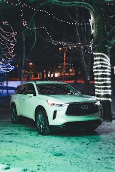 Luxurious Infiniti SUV parked in a snowy, festive scene with Christmas lights at night.