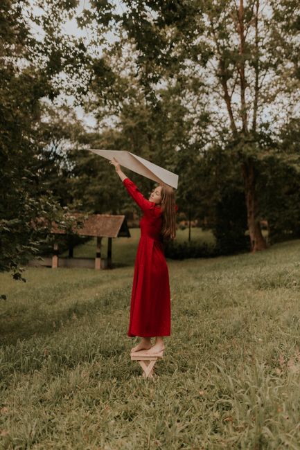 Young woman enjoying a carefree moment in a lush green meadow with a paper airplane.
