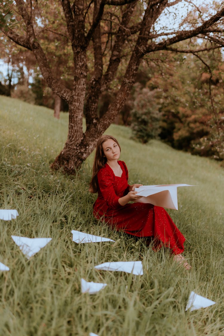 Beautiful Woman In Red Dress Sitting With Paper Airplane In Hands