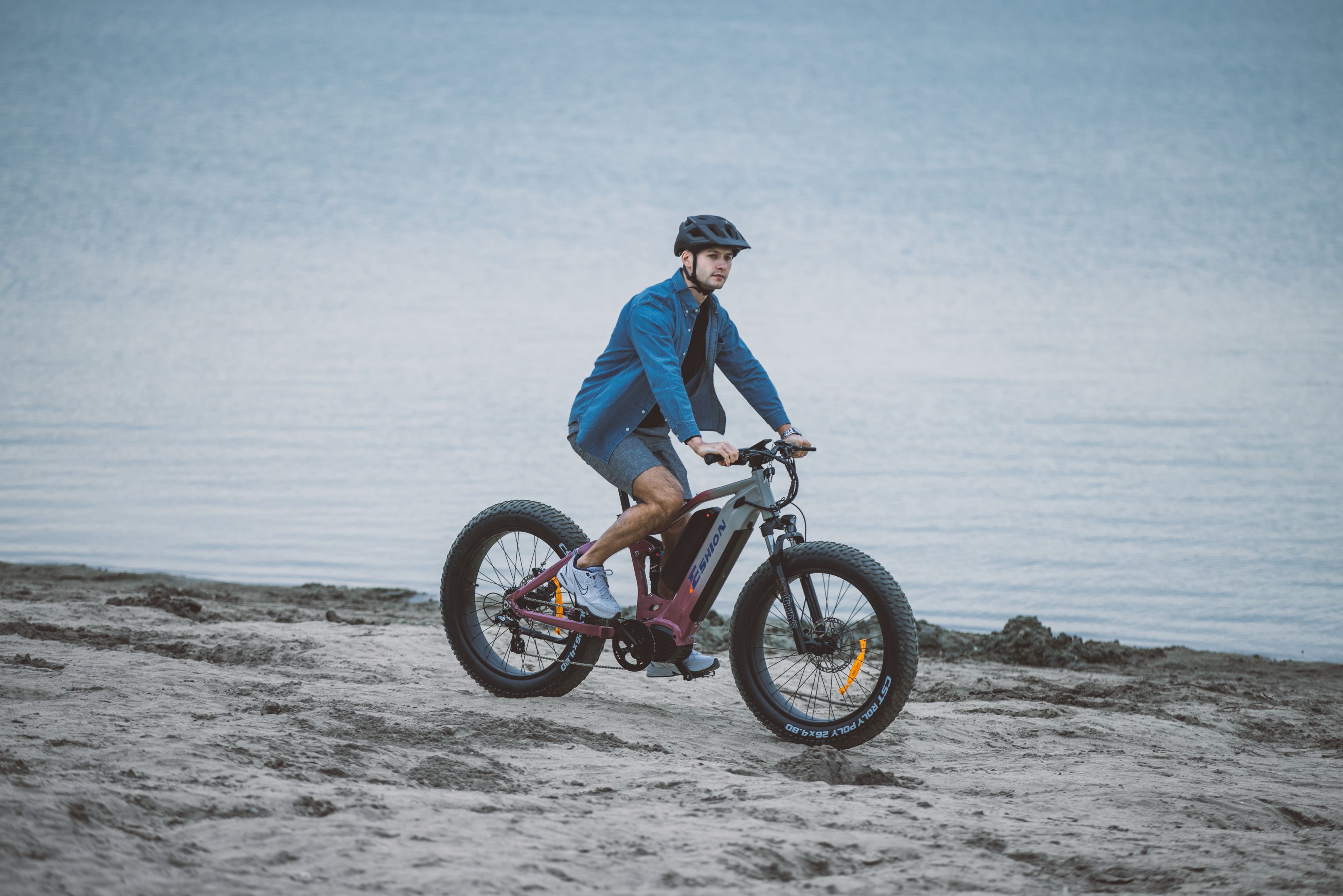 Man riding an electric bike along a sandy beach near the water.