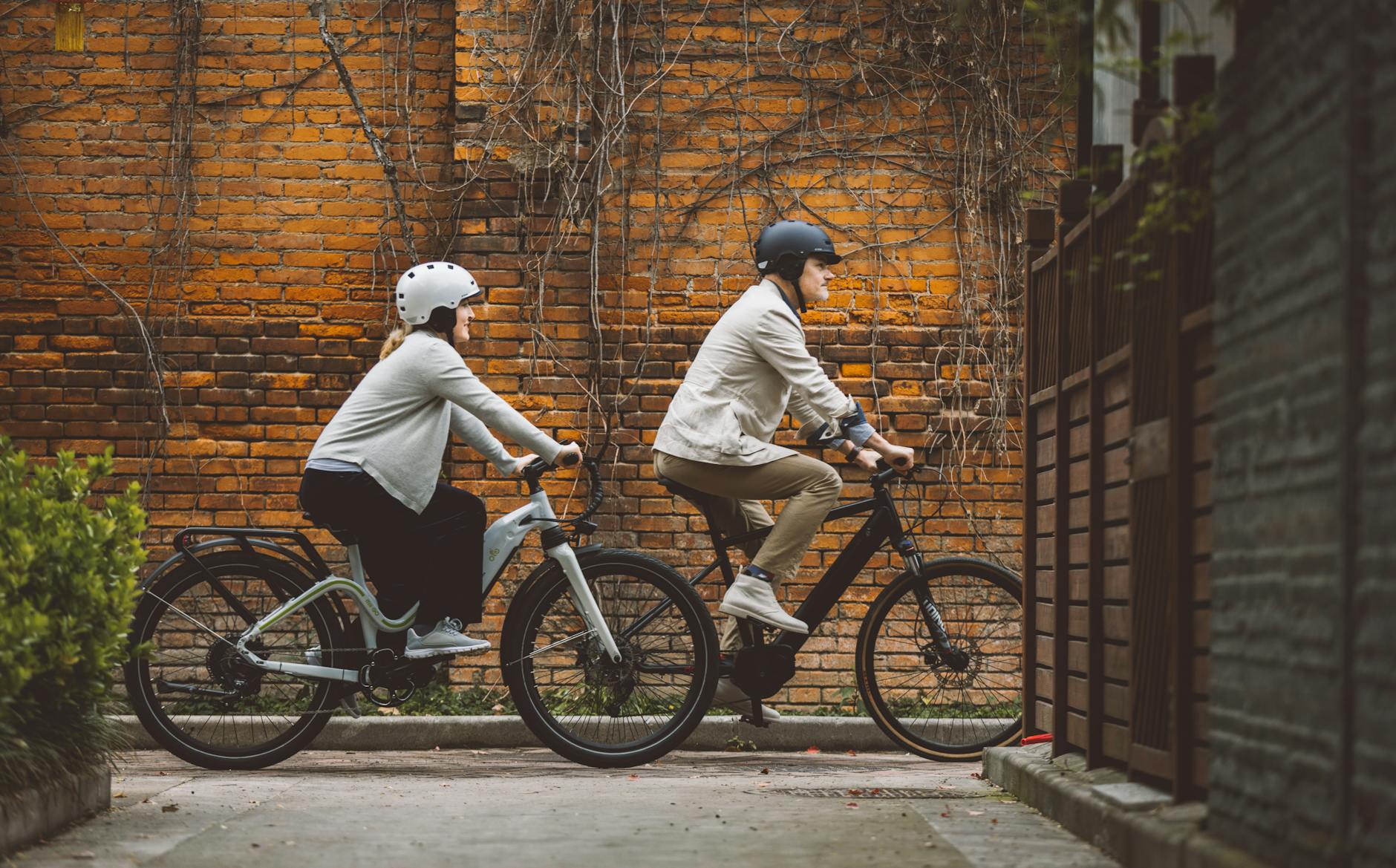 Two people riding bicycles in front of a brick wall