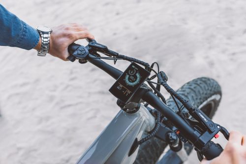 Free A modern electric bicycle handlebar with a touch screen display, featuring riding statistics on a sandy outdoor surface. Stock Photo