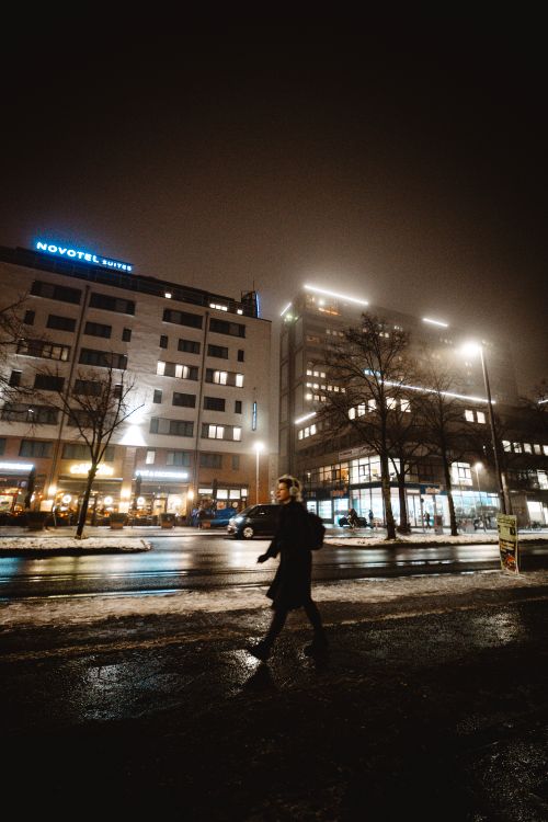 Free A solitary woman walking along a rainy city street in Berlin at night, illuminated by streetlights. Stock Photo