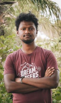 Casual portrait of a young man in a t-shirt with crossed arms, standing outdoors.