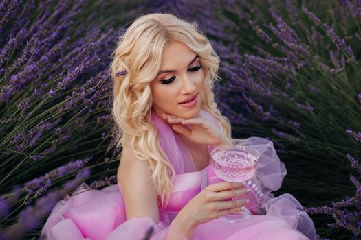 Woman in a lavender field holding a pink drink, embodying relaxation and elegance.