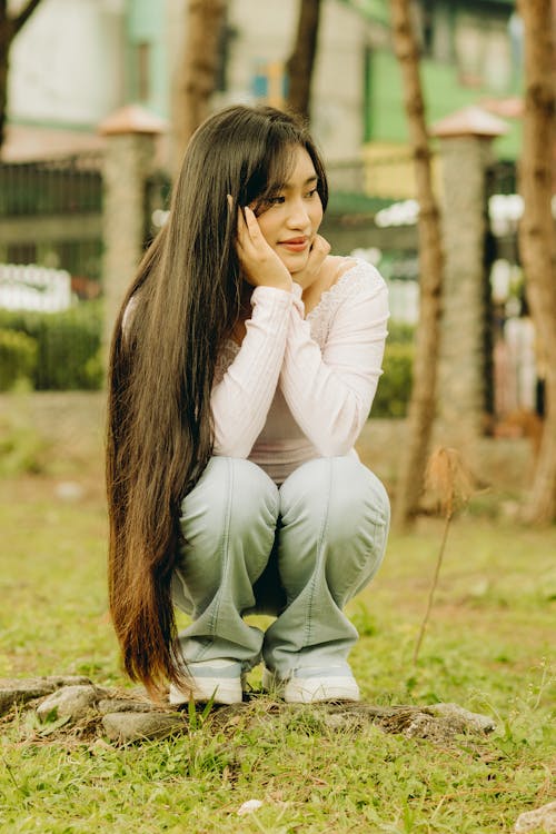 Smiling Woman with Long Hair Squatting with Hands on Cheeks 