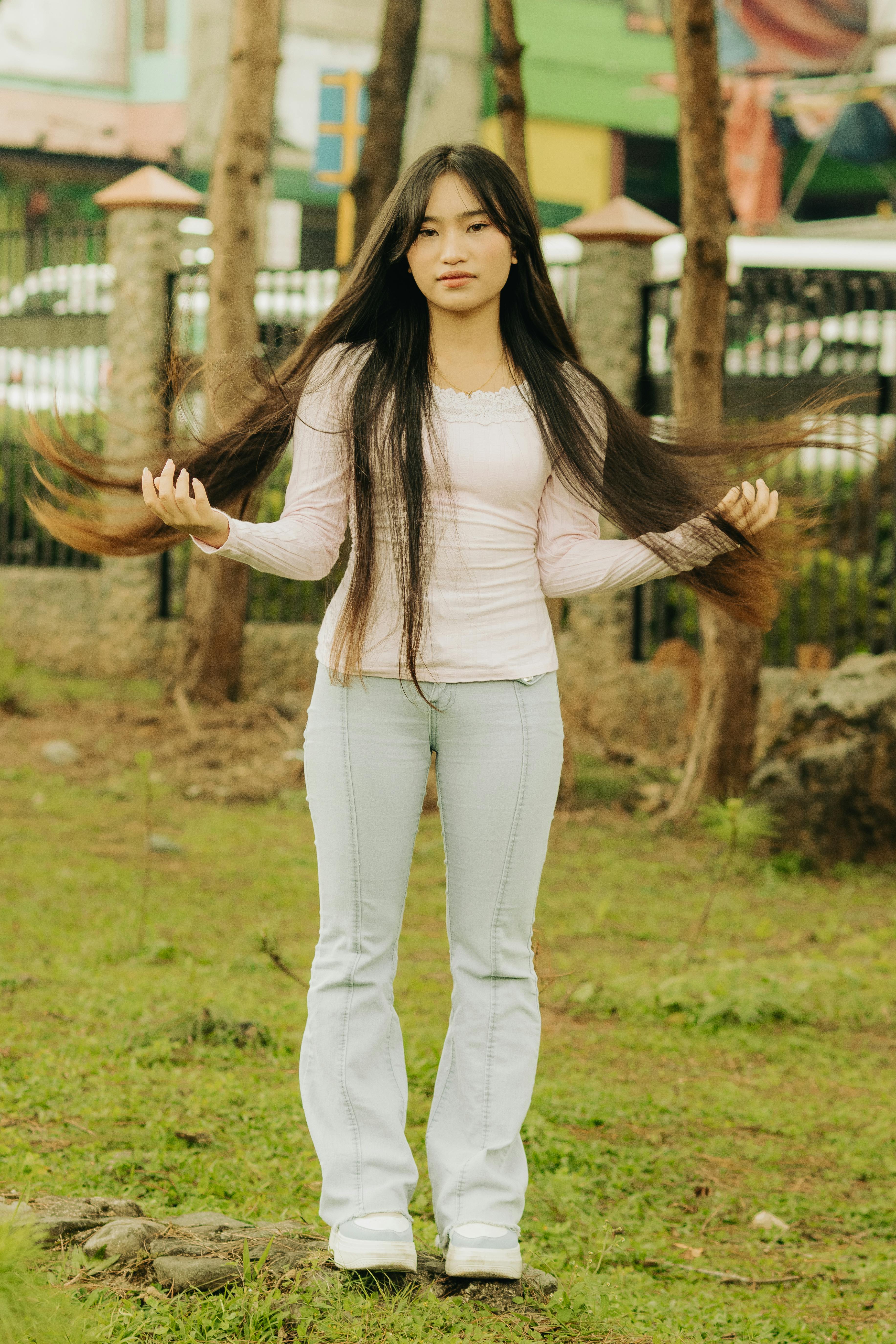 Young woman standing outside in casual fashion, showcasing long hair and a serene expression.
