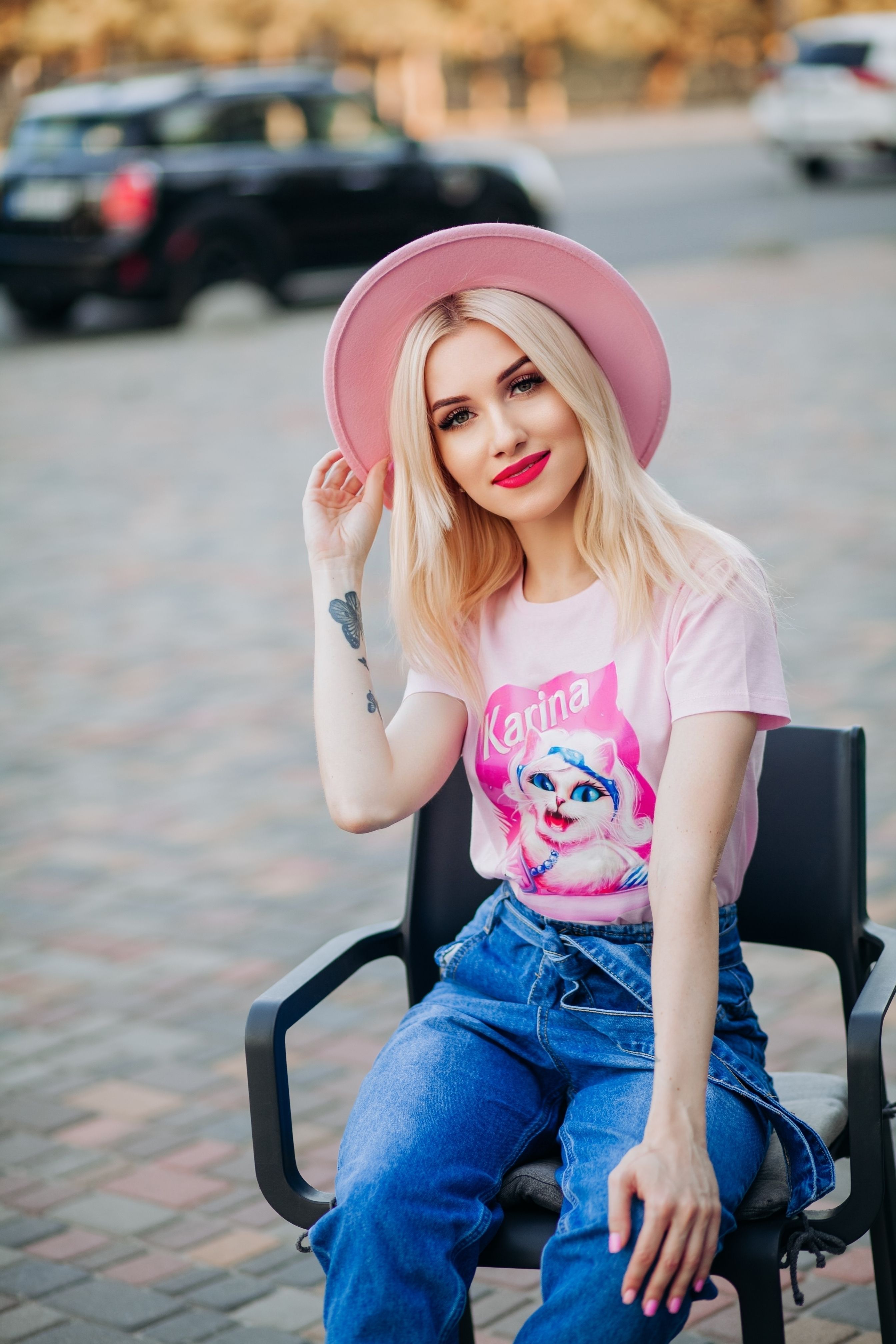 Stylish young woman with pink hat and jeans posing outdoors in an urban setting.