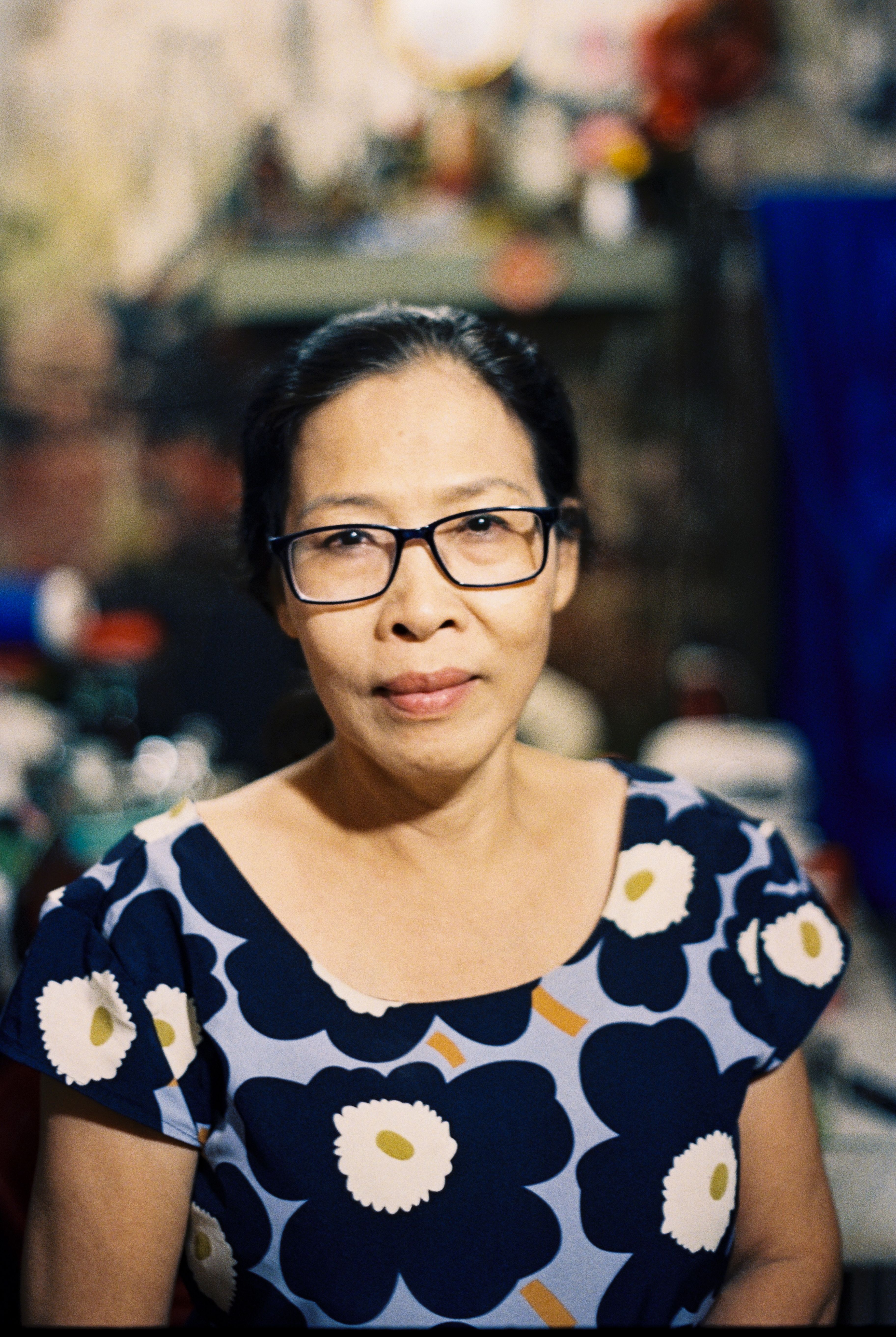 Portrait of a mature woman with eyeglasses, wearing a floral dress, captured indoors.
