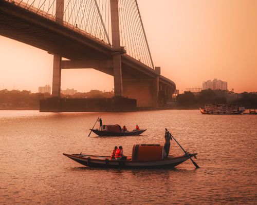 Free Beautiful boats under a suspension bridge during sunset on a tranquil river. Stock Photo