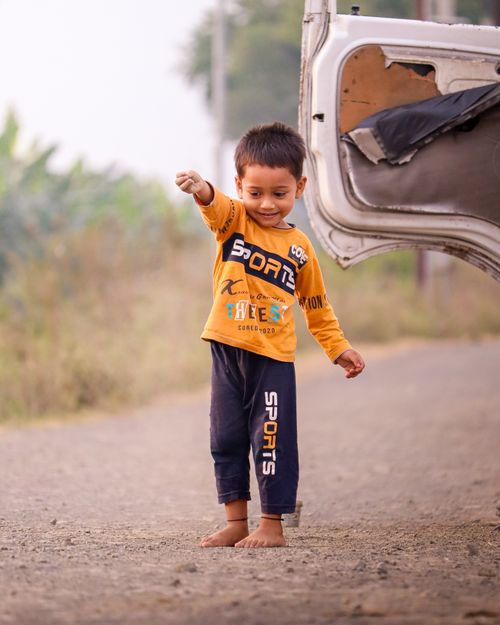 Free A joyful child in sporty attire plays barefoot near an open car door on a rural road. Stock Photo