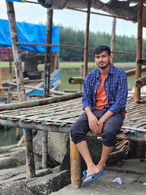 Free A young man sits on a bamboo structure in a serene fishing village in Bangladesh. Stock Photo