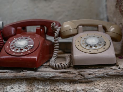 Two vintage rotary phones on a rustic wooden shelf, showcasing retro telecommunication devices.