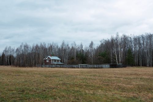 Free A single rural house surrounded by trees and grassland under a cloudy sky. Stock Photo