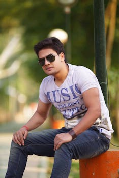 Fashion-forward portrait of a young man in sunglasses sitting outdoors, exuding confidence.