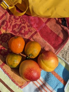 Fresh fruits like oranges and peaches on colorful beach towels, sunlit and vibrant.