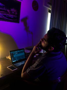 A man sitting at a desk with a laptop under moody lighting setup, evoking late-night work vibes.