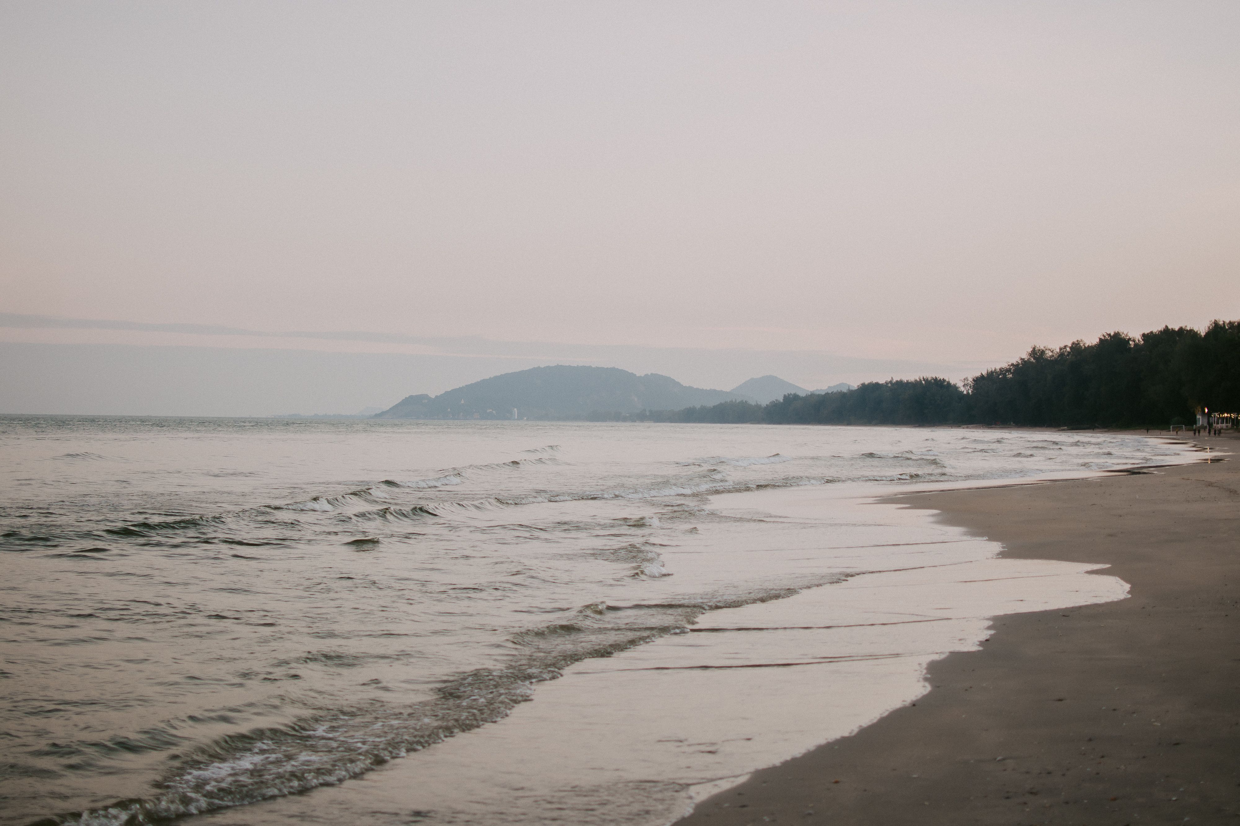 A peaceful coastline with soft waves and distant hills at dusk, offering tranquility.