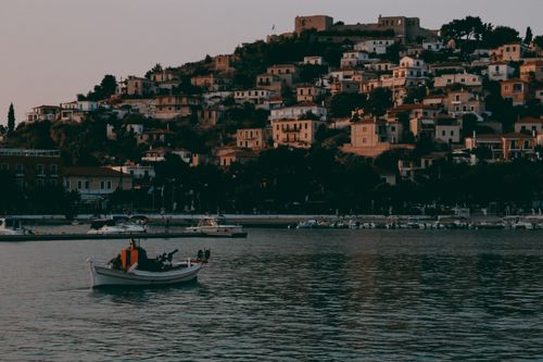 Free A serene boat ride with a backdrop of Paralio Astros, Greece, at dusk. Calm waters and historic townscape. Stock Photo