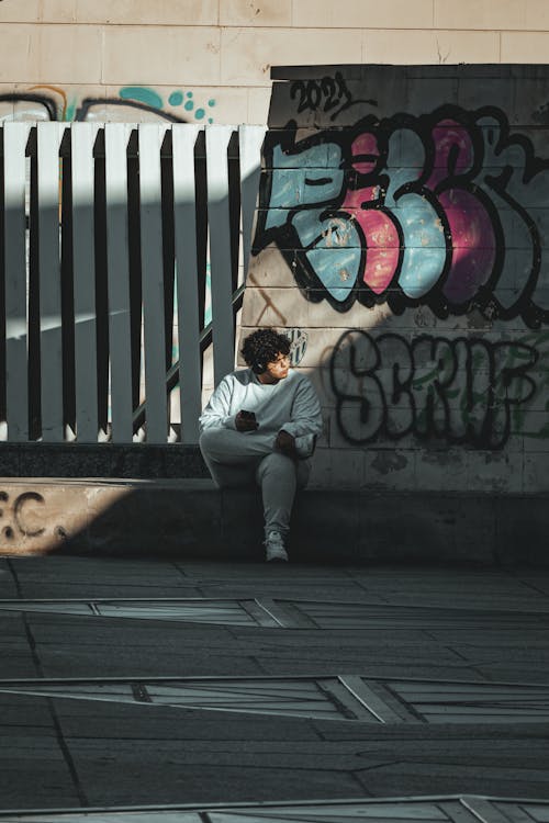 Man Sitting on a Street in Front of Graffiti 