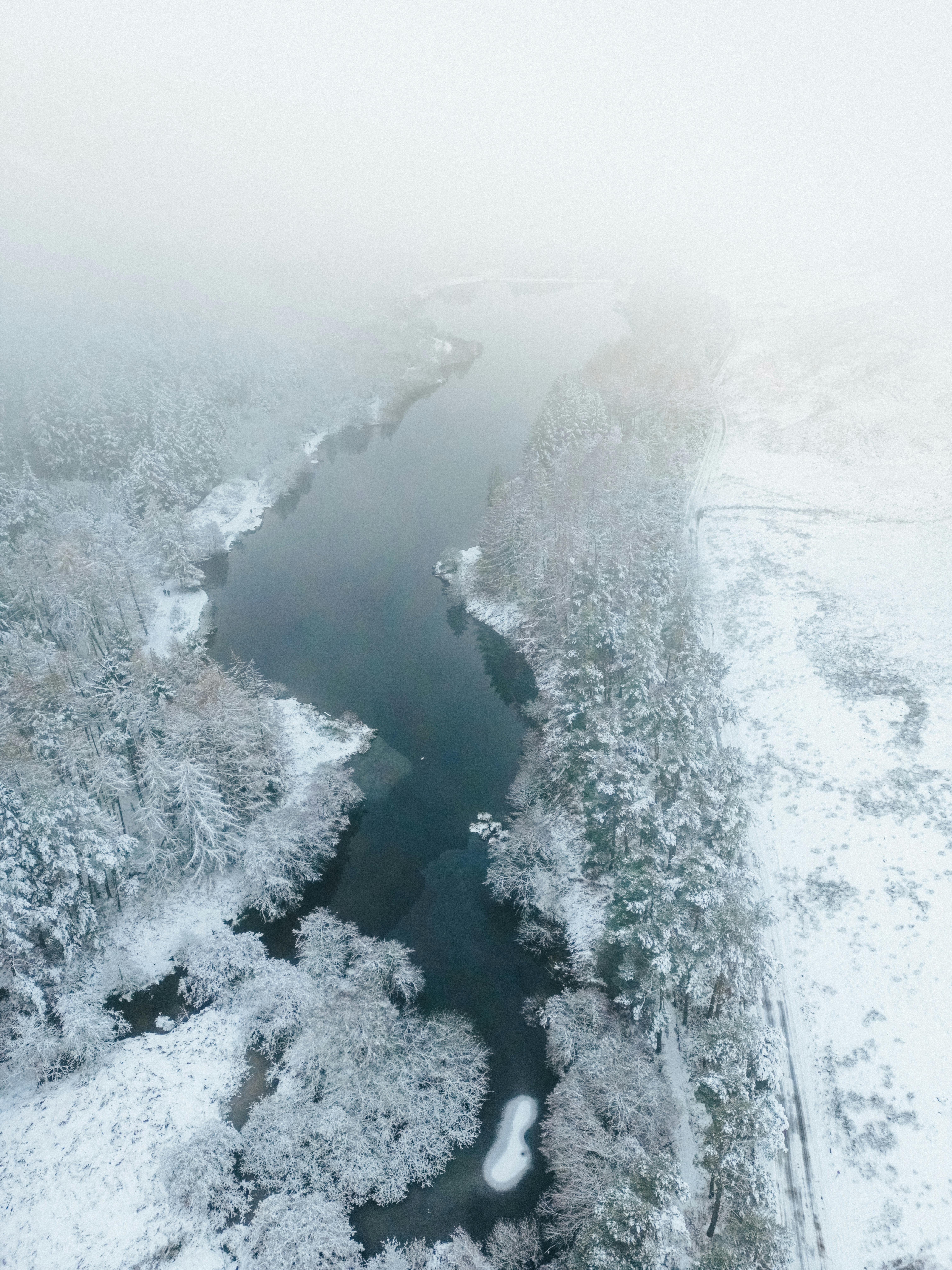 Breathtaking aerial view of a snow-covered river landscape shrouded in fog.