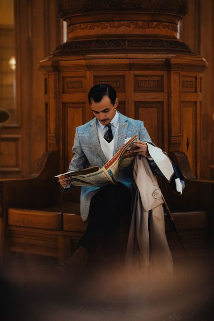 A stylish man in a classic suit reading a newspaper in a vintage indoor setting.