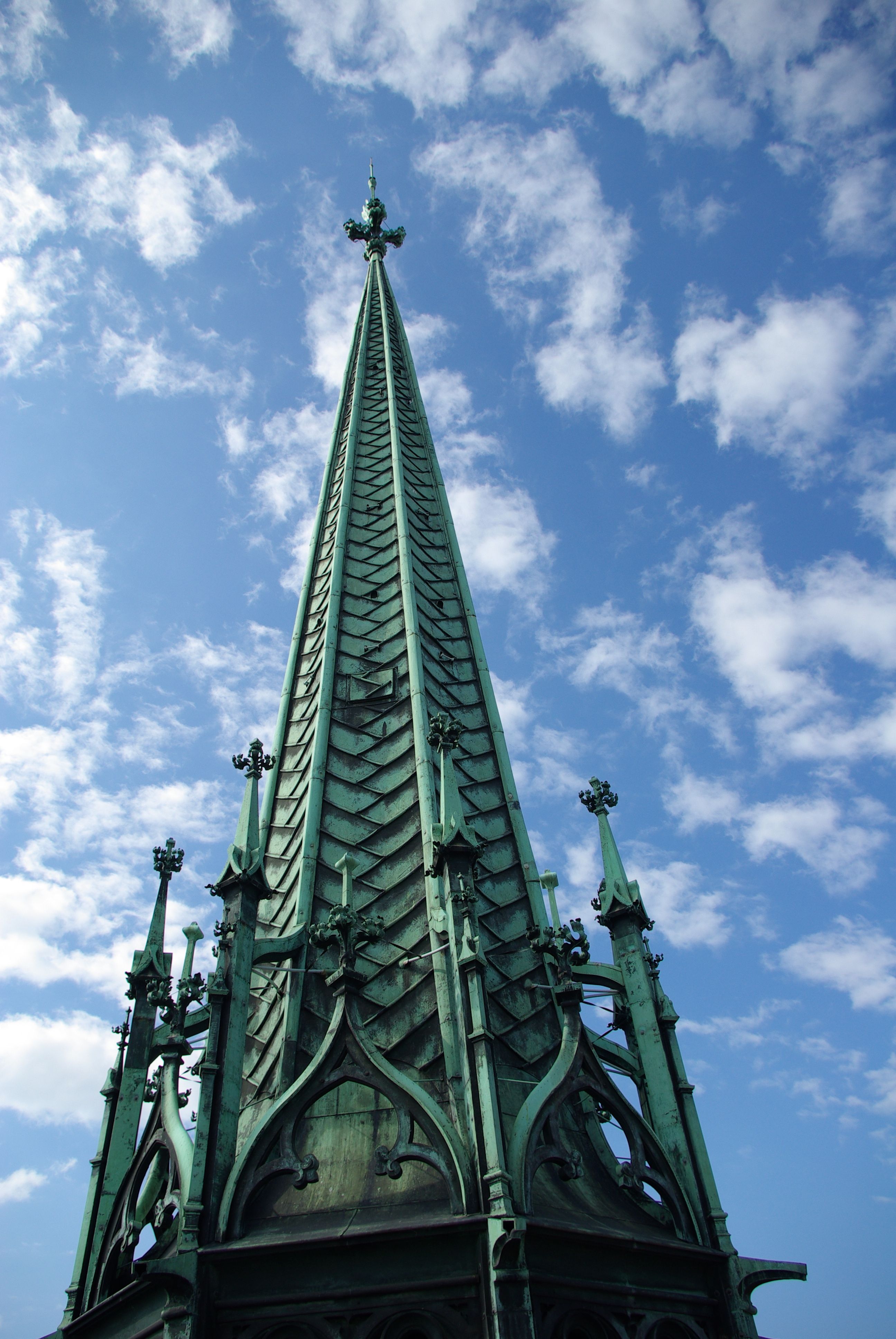 Dramatic perspective of St. Pierre Cathedral's intricate spire reaching into a cloud-dotted sky.