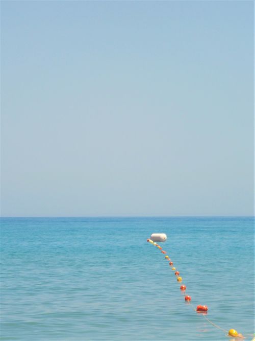 Free A serene seascape with orange buoys leading into the horizon over calm blue waters, under a clear sky. Stock Photo