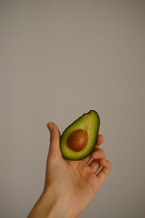 Free Close-up of a hand holding a fresh avocado half with seed, simple and natural composition. Stock Photo