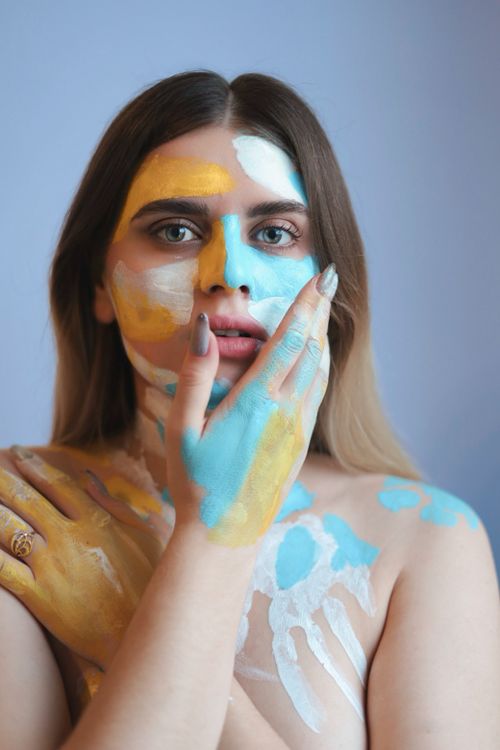 Free Artistic portrait of a woman with vibrant face paint in blue, yellow, and white tones. Stock Photo