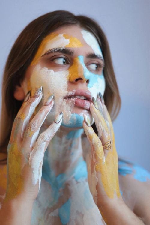 Free Artistic studio portrait of a woman with colorful paint on her face, expressing creativity and emotion. Stock Photo
