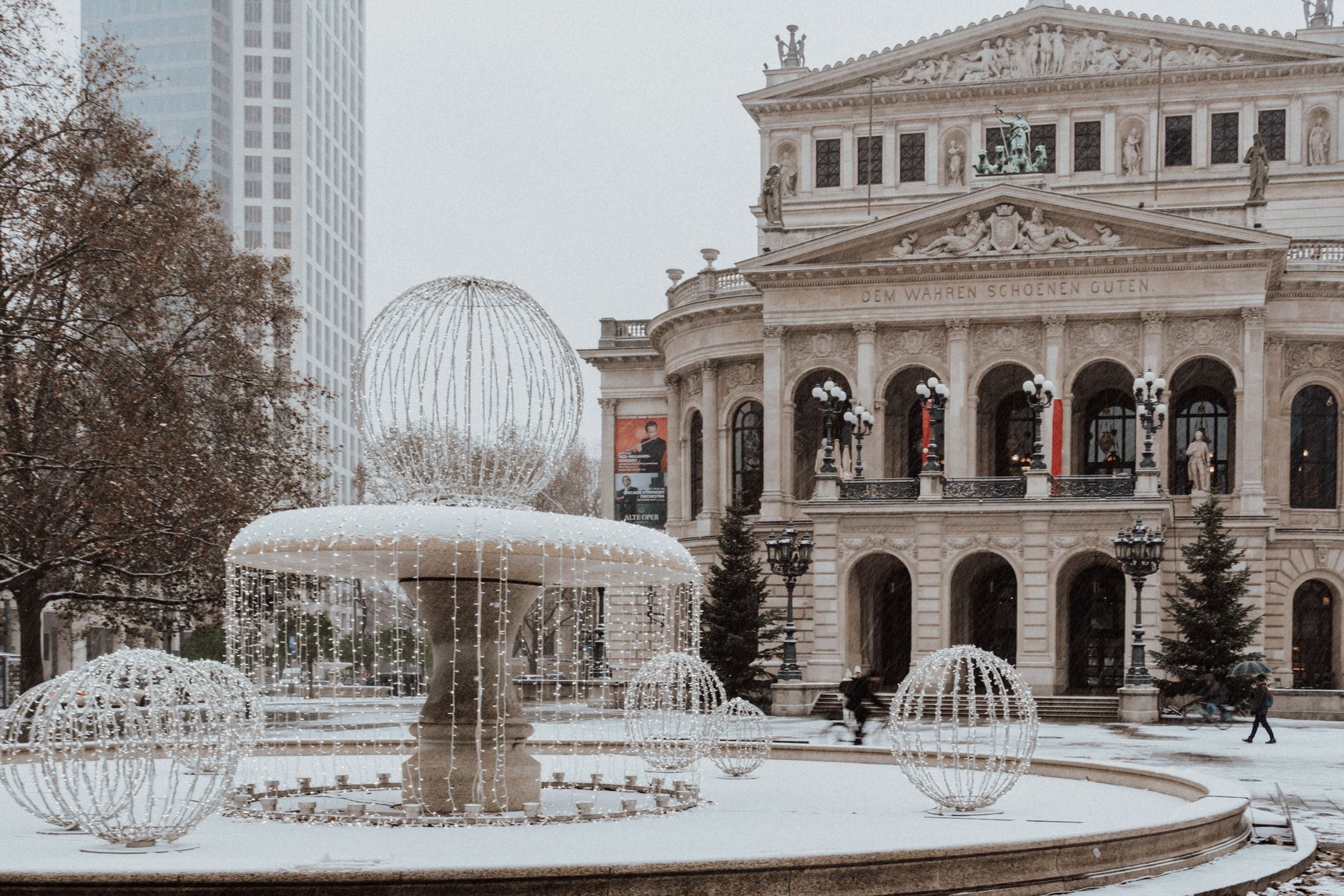 Snow-covered fountain and opera house in a European city square during winter.