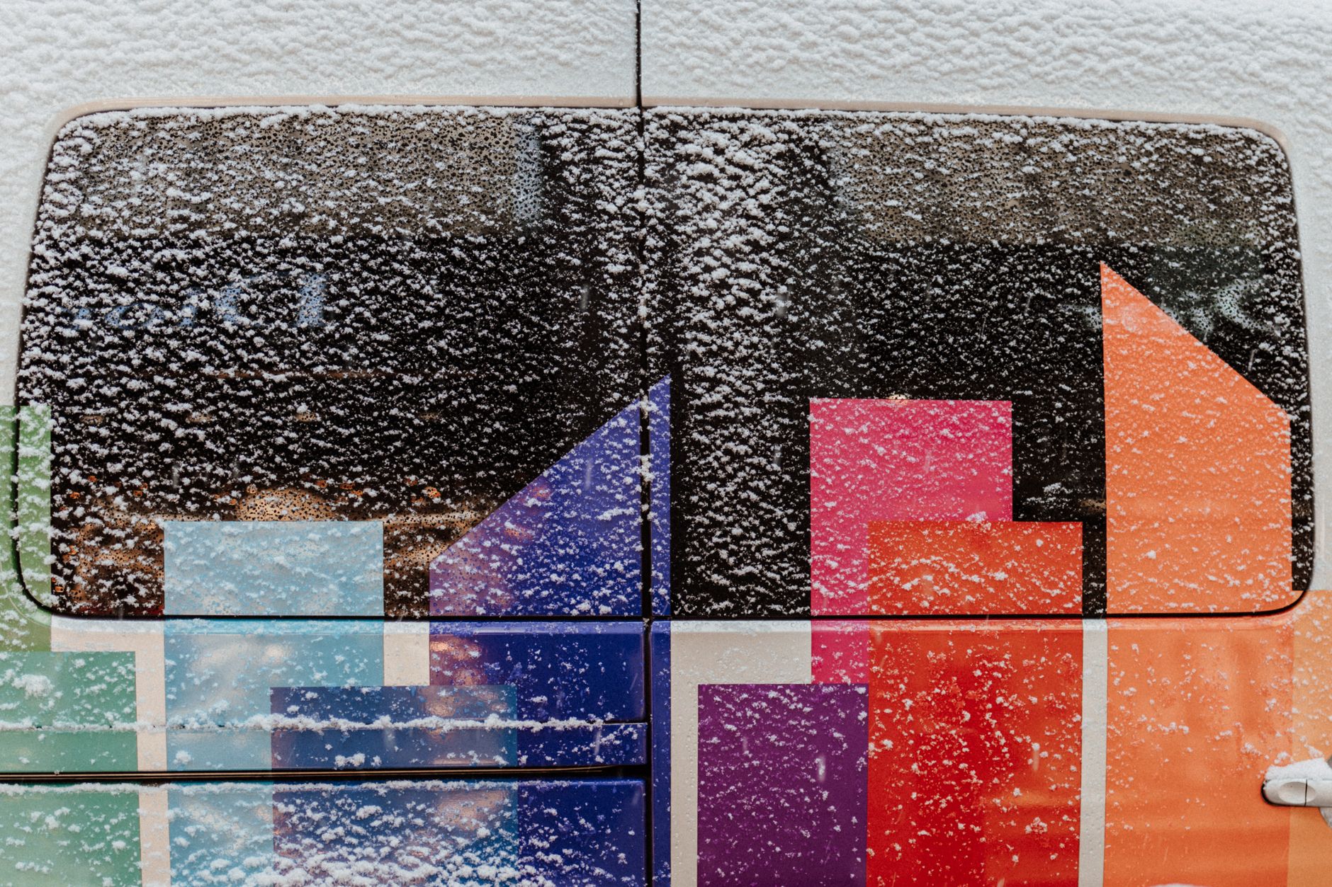 Snow-covered window on a vibrant vehicle, highlighting winter's chill against colorful patterns.