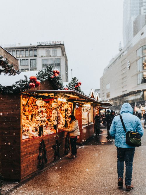 Free Festive Christmas market stalls with people shopping in a snowy urban setting. Stock Photo