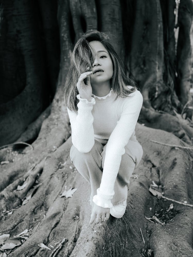 Grayscale Shot Of A Woman Crouching On Tree Roots