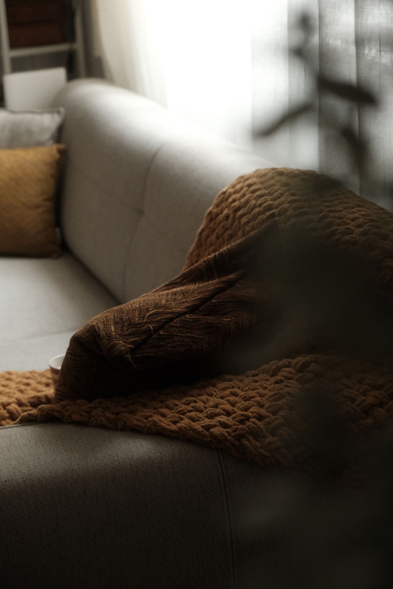 Chunky chocolate brown knit throw and mustard pillow on a light gray sofa