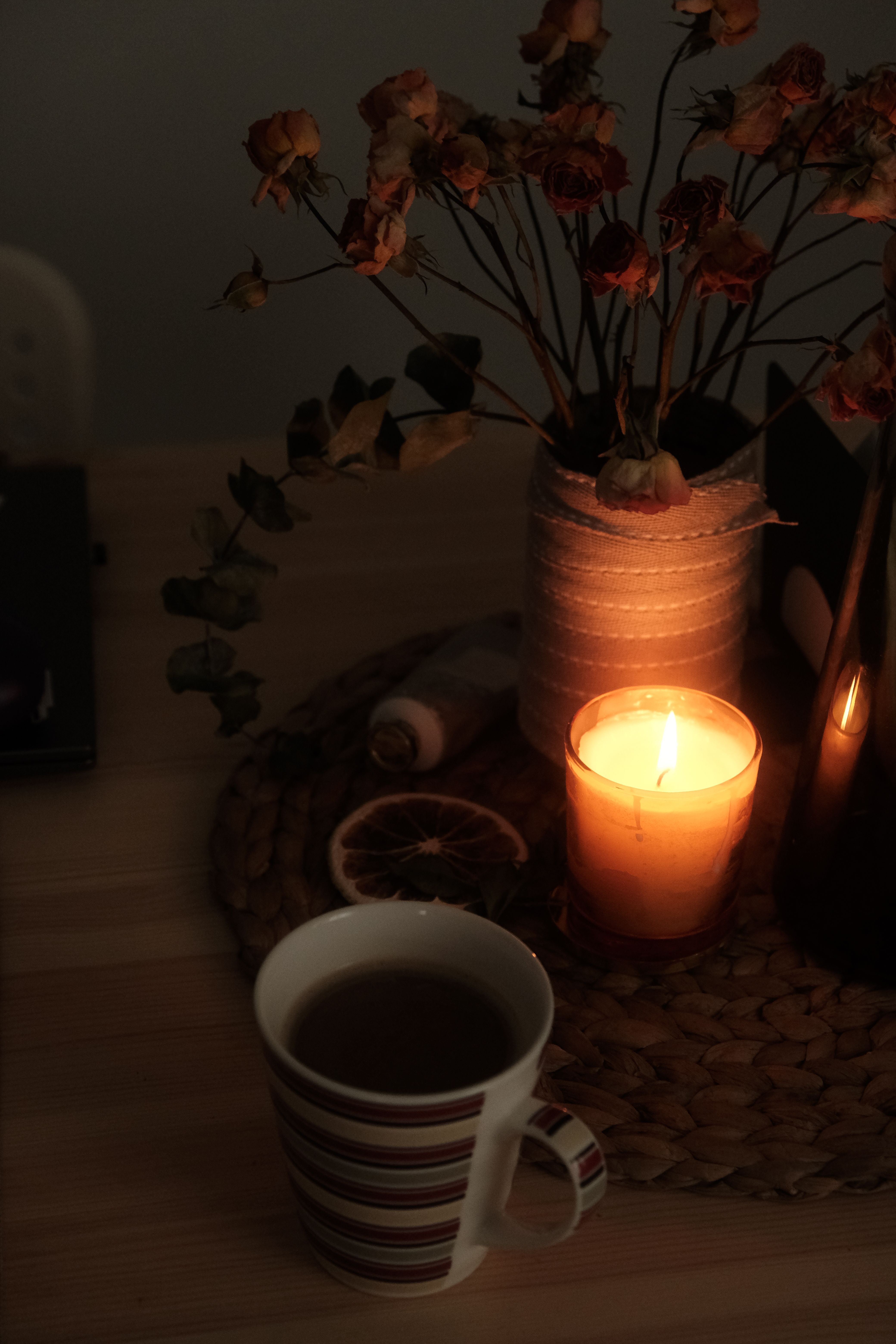 Free Warm candlelight on a table with a mug of tea and dried flowers in a vase, creating a cozy atmosphere. Stock Photo