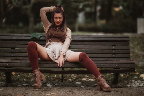 Young Woman in a Skirt Sitting on a Bench in a Park 