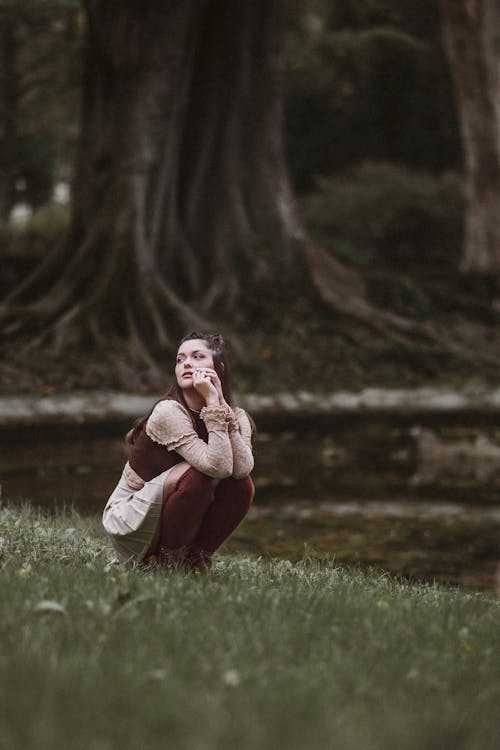 A Woman Crouching on the Grass in a Park 