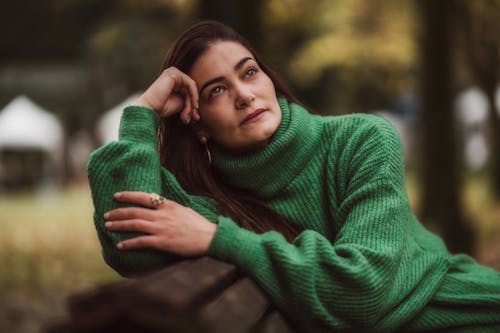 Young Woman in a Green Sweater Sitting on a Bench in a Park 