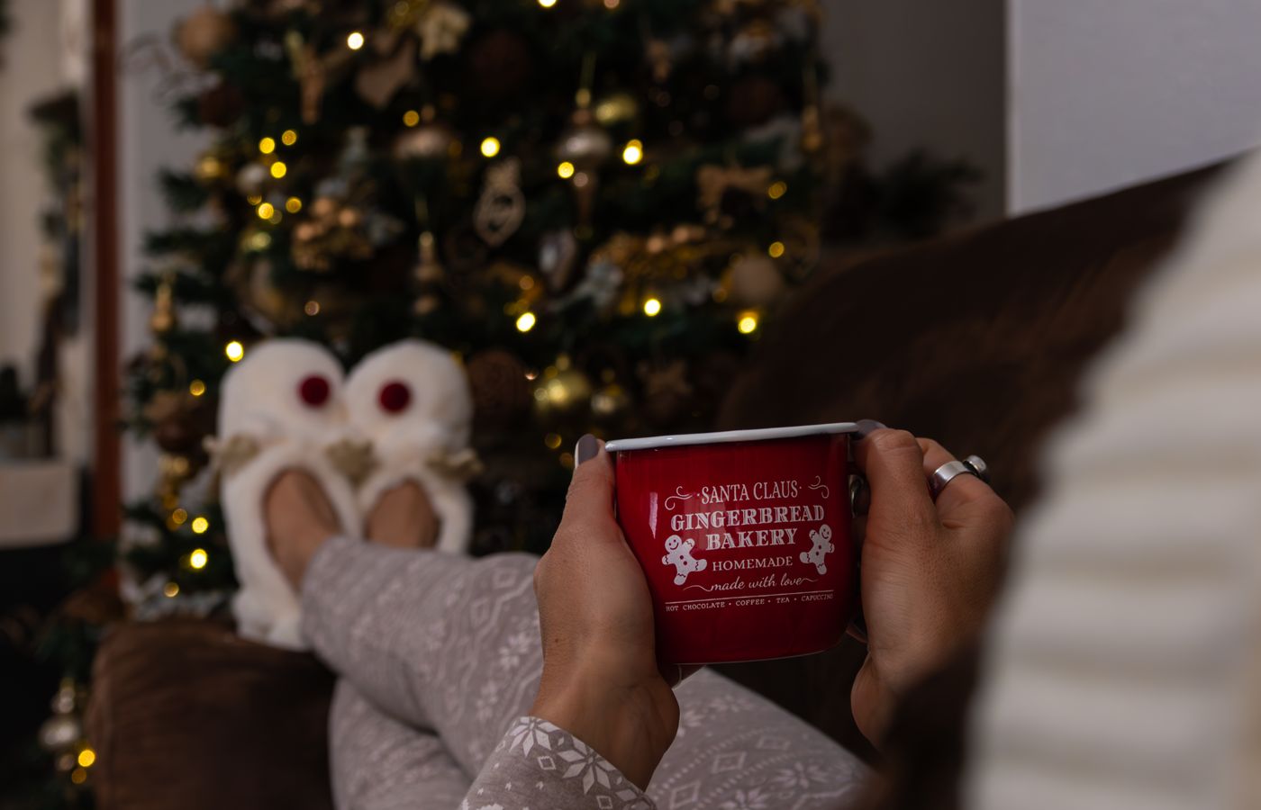Relaxing by the Christmas tree with a hot drink in festive pajamas and slippers.