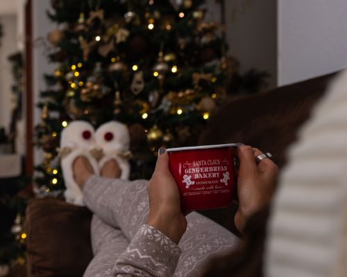 Free Relaxing by the Christmas tree with a hot drink in festive pajamas and slippers. Stock Photo