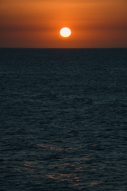 Free A captivating sunset over the vast ocean with golden hues reflecting on the water's surface. Stock Photo