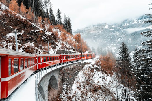 A red train navigates a snowy mountain landscape in winter, surrounded by forests.
