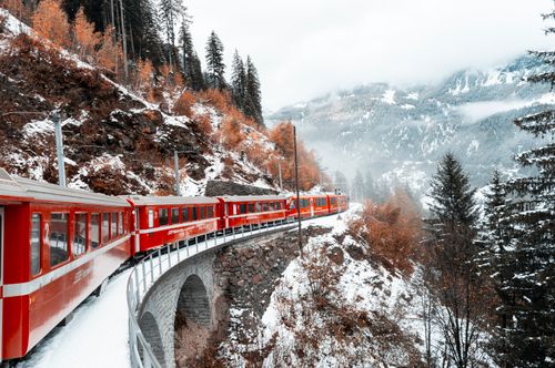 Free A red train navigates a snowy mountain landscape in winter, surrounded by forests. Stock Photo